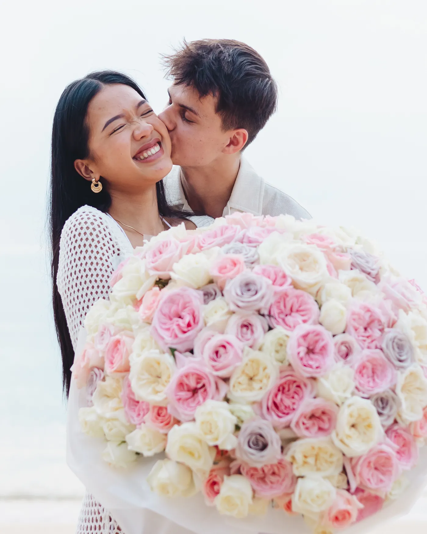 Gabriel kissing Thipwaree's cheek as she holds a huge bouquet of roses